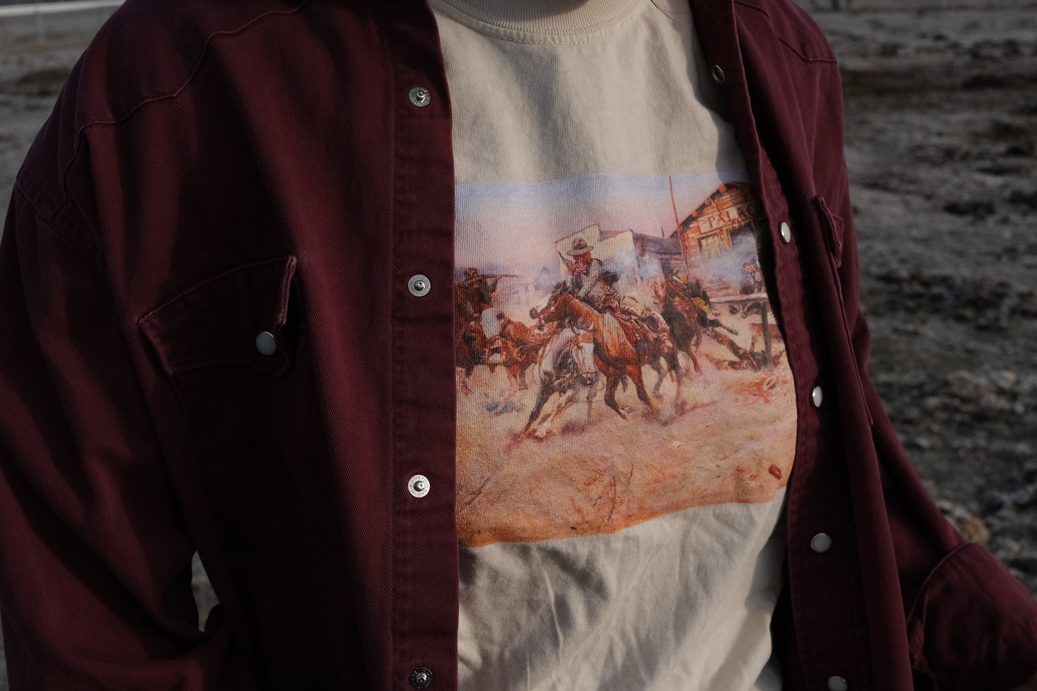 Beige T‑shirt featuring a cowgirl wearing a Charles Marion Russell’s Smoke of a .45 t-shirt depicting a cowboy firing his revolver in a tense Western scene.